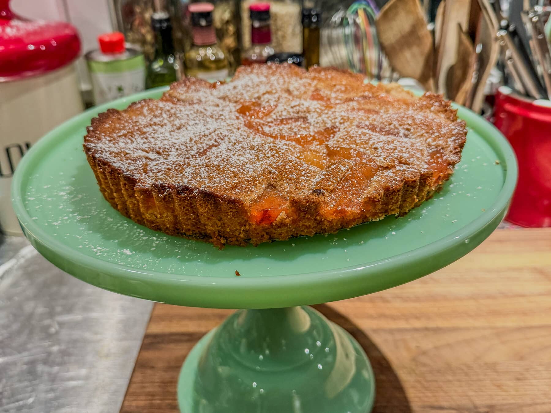 A brown butter cake with pieces of quince in it on a jadeite cake stand.